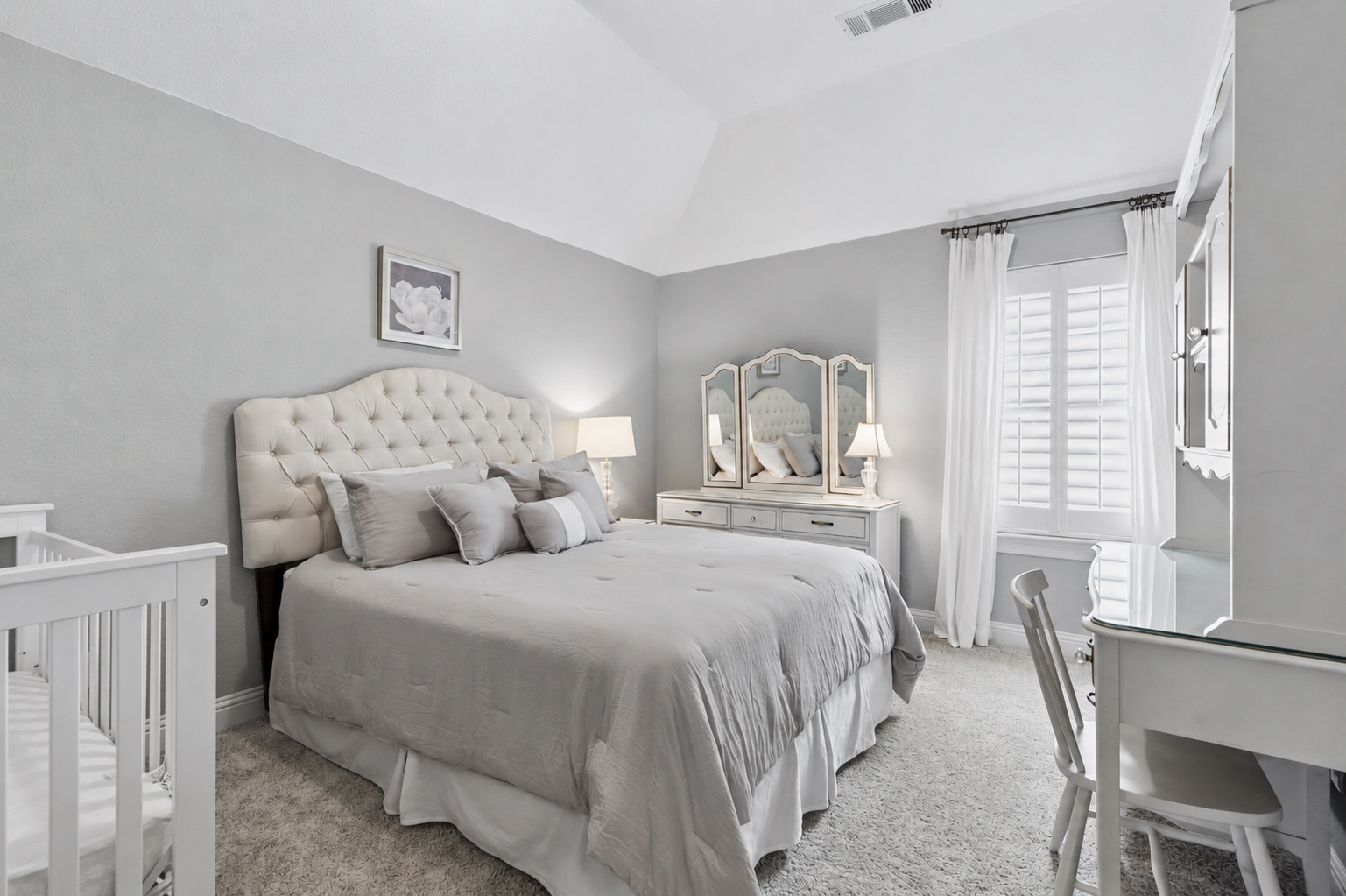 Upstairs bedroom with tufted headboard, vanity mirror, and plantation shutters